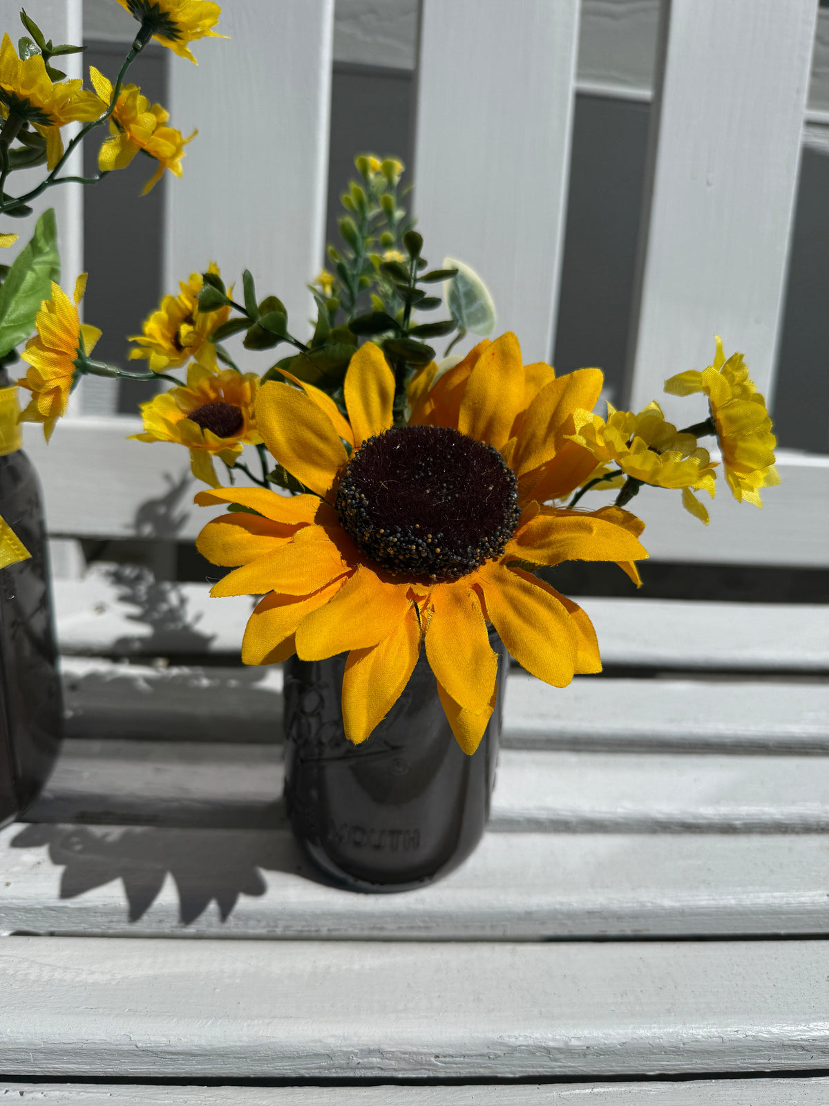 Barking Gardener farmhouse faux sunflower arrangement in a dark glass mason jar on a white wooden bench