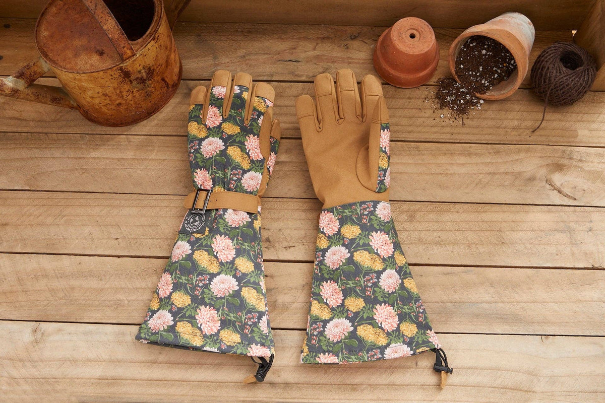 Barking Gardener Arm Saver Gloves with floral print, extra-long cuffs, and tan synthetic leather palms on wood table.