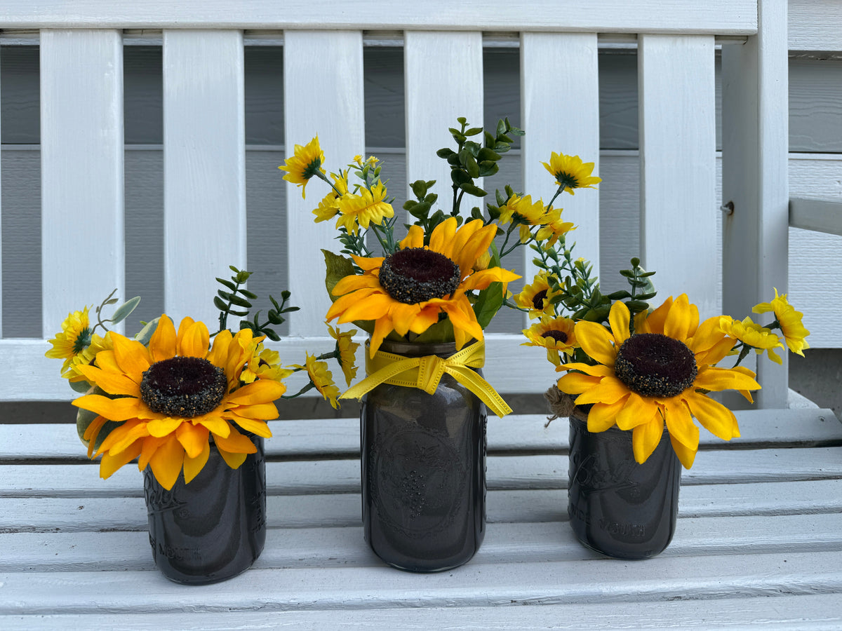 Barking Gardener farmhouse faux sunflower arrangement in three dark grey mason jars with yellow ribbon accents