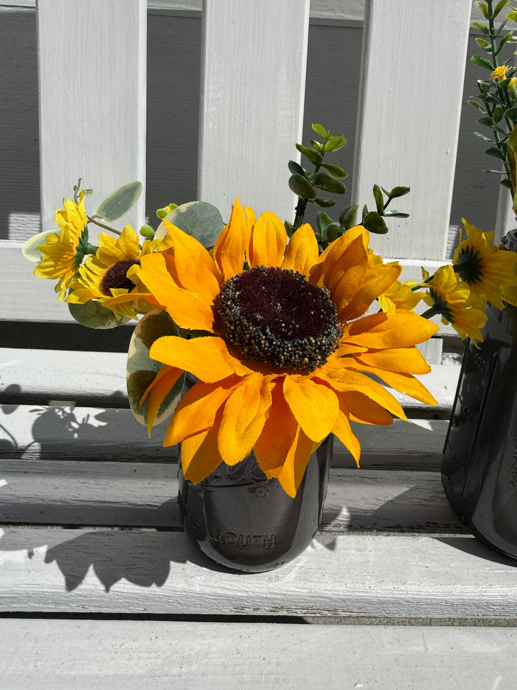 Barking Gardener farmhouse faux sunflower arrangement in a dark glass mason jar on a white wooden bench