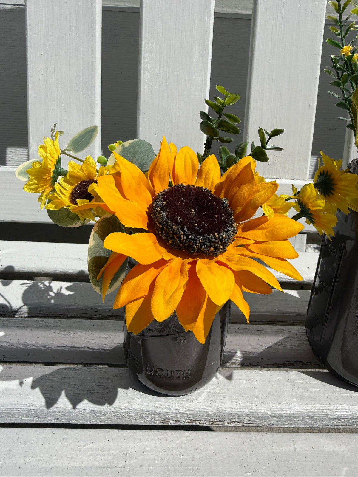 Barking Gardener farmhouse faux sunflower arrangement in a dark glass mason jar on a white wooden bench